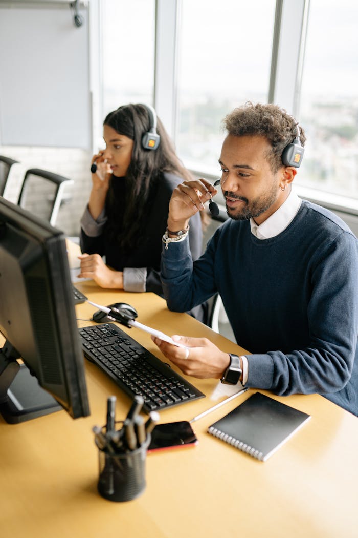 about-us Two diverse call center agents working together at their desks with headsets in a bright office.